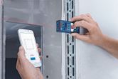 Person uses a laser measure and smartphone app to record measurements on a wall.