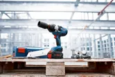 Cordless impact wrench on a wooden pallet with bolts at a construction site.