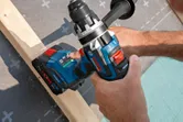 A person uses a cordless drill driver to work on a wooden beam.