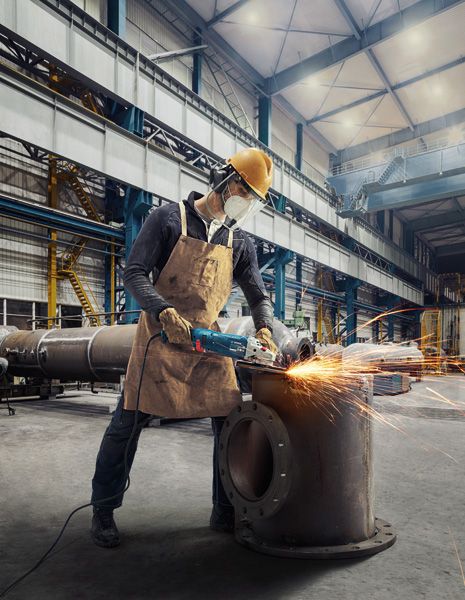 GWS 24-180 JZ A person wearing safety equipment uses a power grinder to cut metal, creating sparks.