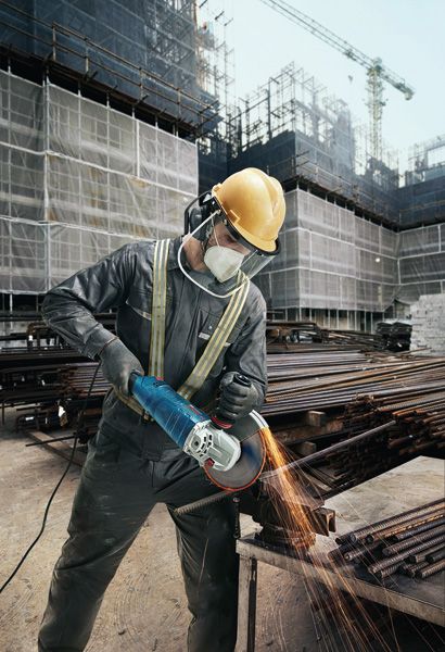 GWS 24-180 JZ A person wearing safety equipment grinds metal bars with an angle grinder at a construction site.