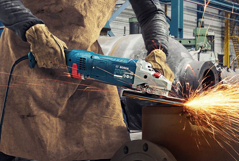 A person wearing safety equipment grinds metal, producing bright sparks.
