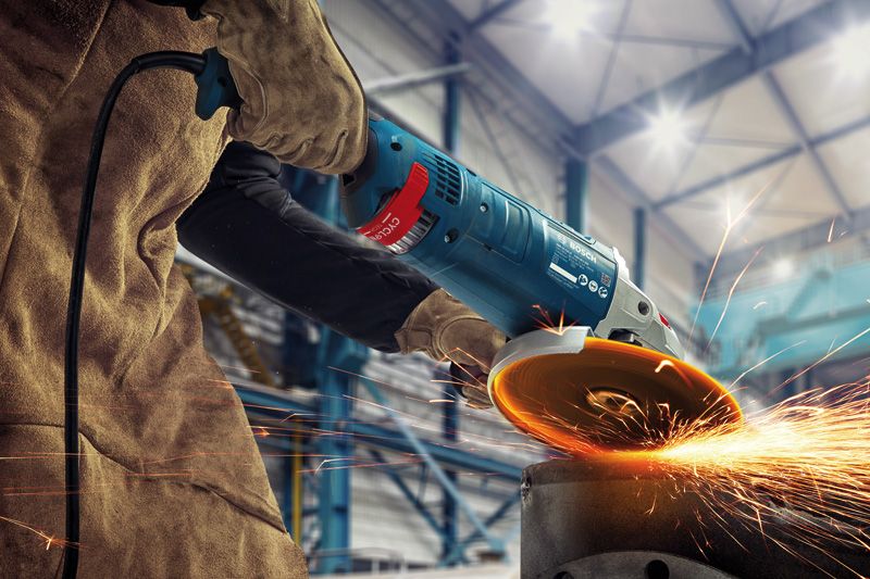 GWS 24-180 JZ A person wearing safety equipment grinds metal, producing bright sparks in a workshop.