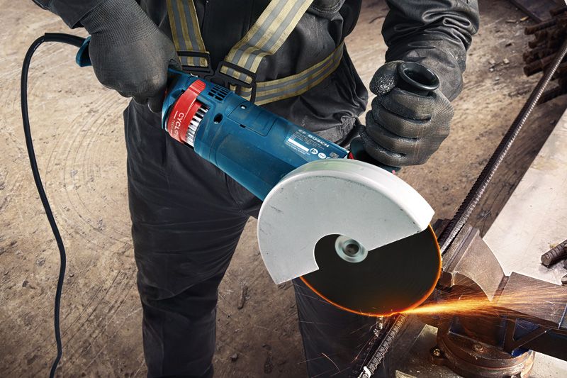 GWS 24-180 JZ A person wearing safety equipment cuts metal rebar with an angle grinder, creating sparks.