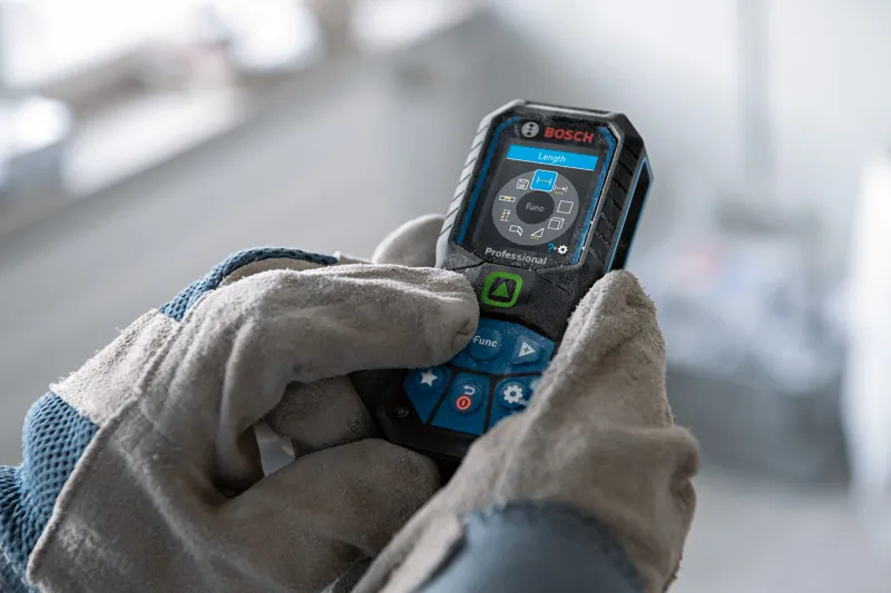 Person wearing safety equipment operates a laser measure with a digital display.