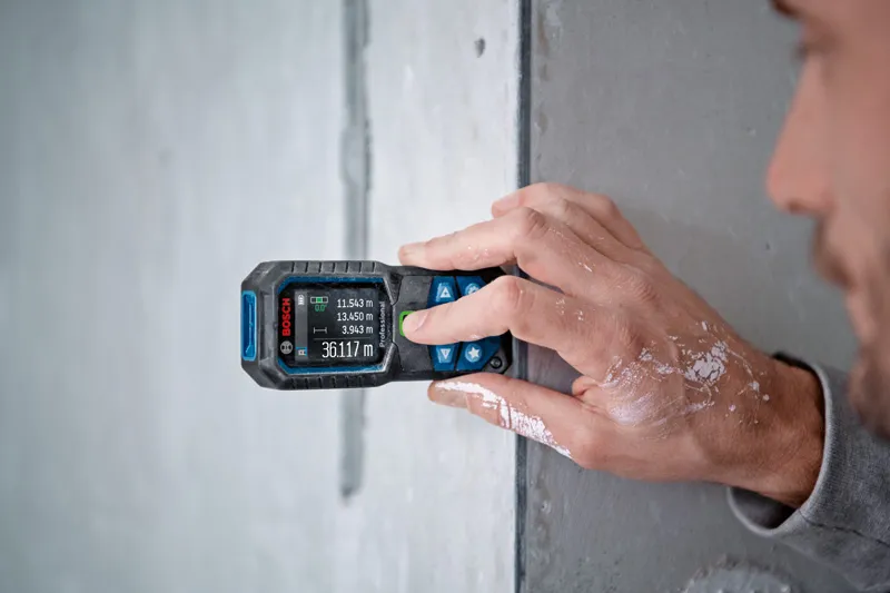 Person measuring wall distance with a laser measure, paint visible on their hand.