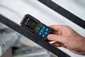 A person measures an angle on a metal beam using a laser measure.