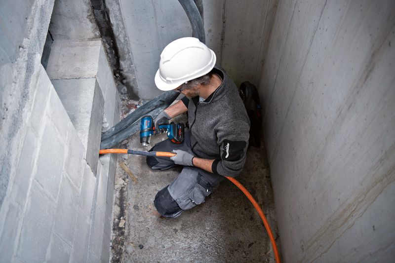 A person wearing safety equipment uses a cordless heat gun to work on an orange cable.