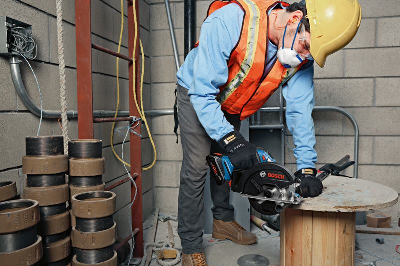 GKM 18V-50 A person wearing safety equipment cuts wood with a handheld saw on a construction site.