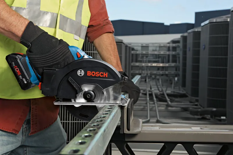 A person wearing safety equipment cuts a metal beam with a cordless circular saw.