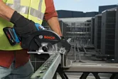 A person wearing safety equipment cuts a metal beam with a cordless circular saw.