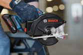 A person wearing safety equipment cuts a metal pipe with a cordless circular saw.