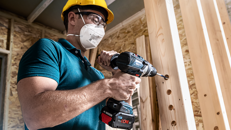 EXPERT Self Cut Speed Spade Drill Bit 12 x 152 mm Person wearing safety equipment drills holes in wooden beams.