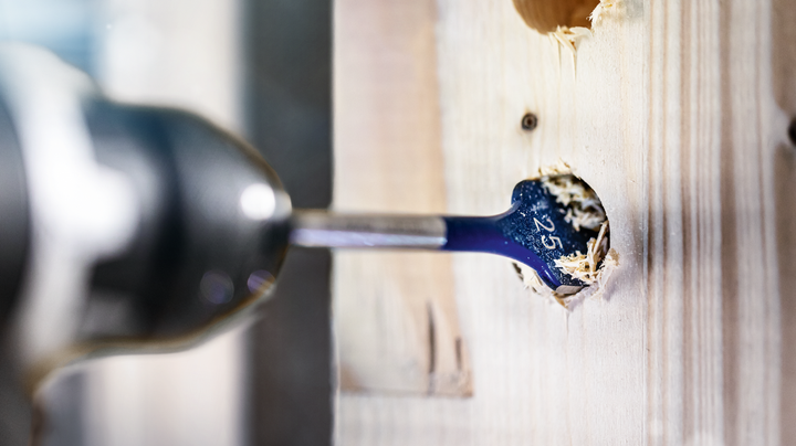Flat drill bit boring a large hole through a wooden board.