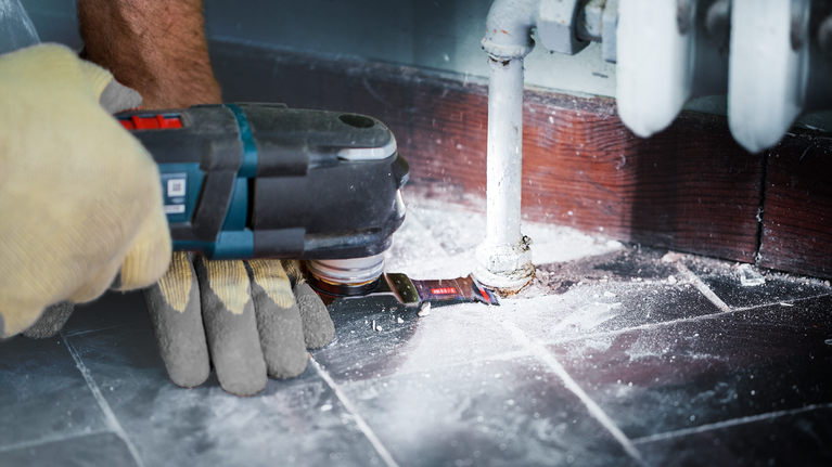 EXPERT MetalMax AIZ 32 AIT Multitool Blade 40 x 32 mm A person wearing safety equipment uses a power tool to cut flooring around a pipe.