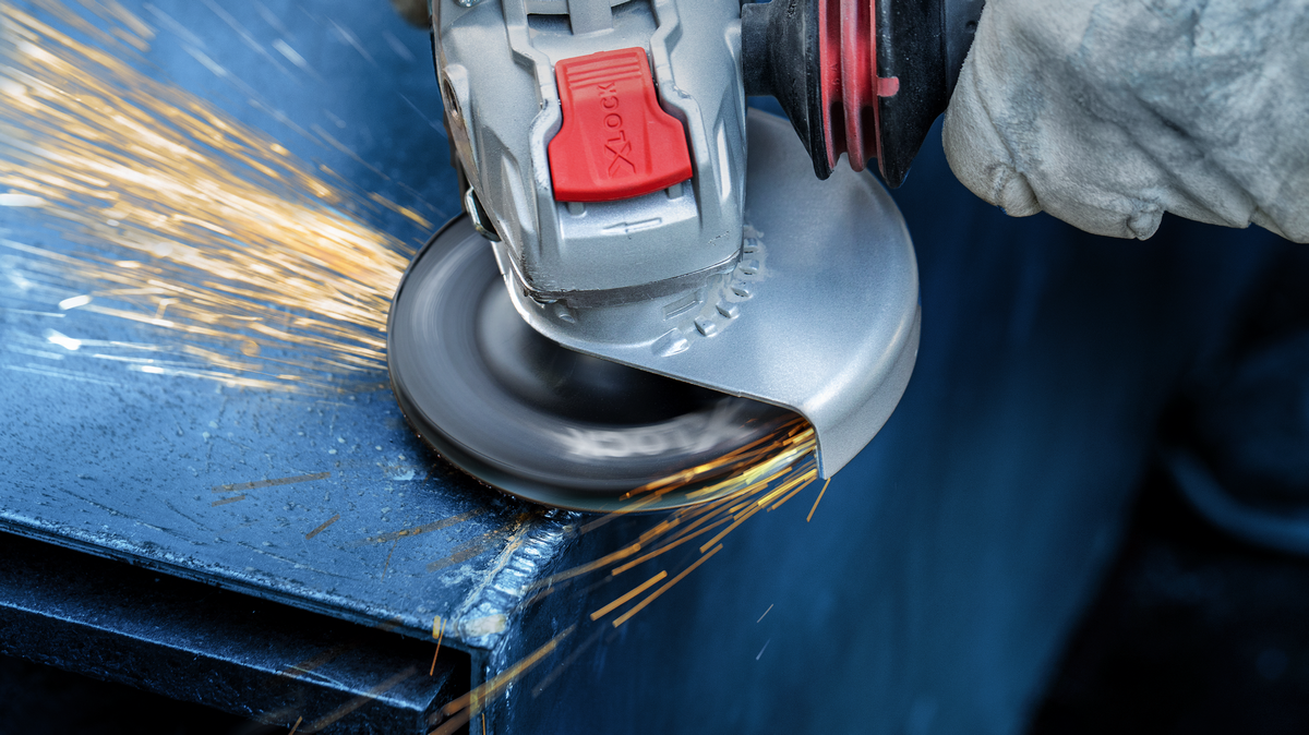 Person wearing safety equipment grinds metal, creating sparks along the edge.