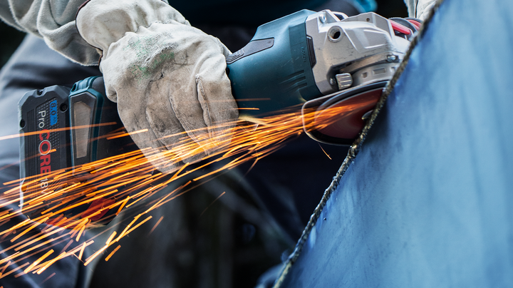 Object #200360616: 2793250_web_004 A worker wearing safety equipment grinds metal, producing bright sparks.