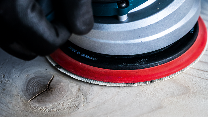 Person wearing safety equipment sands a wooden surface with a power sander.