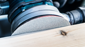 Orbital sander smoothing a wooden plank.