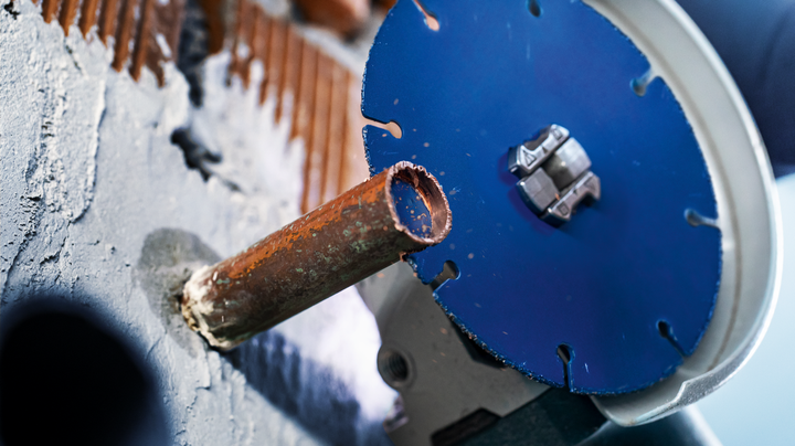 Object #200360639: 2793276_web_003 A metal pipe is being cut through a wall using a circular power saw blade.
