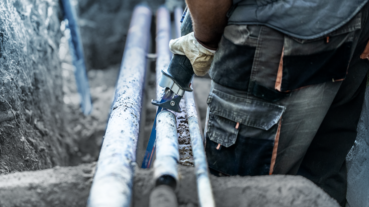 Worker wearing safety equipment cuts a metal pipe with a reciprocating saw.