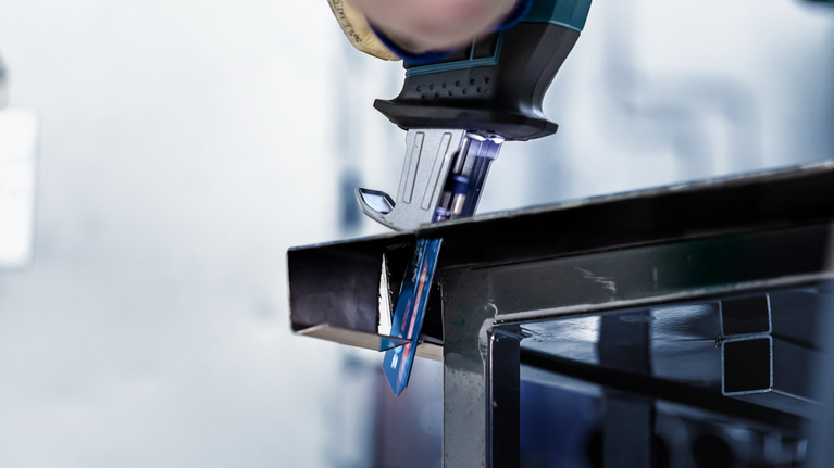 Person using a jigsaw to cut a metal beam.