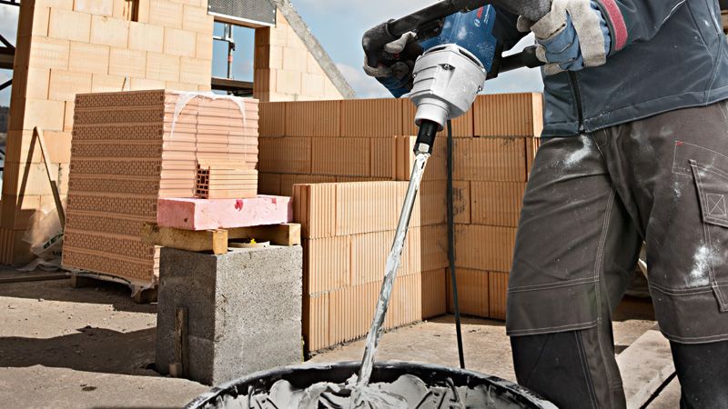 GRW 12 E A person wearing safety equipment mixes cement with a stirring mechanism at a construction site.
