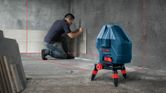 A person installs wall tiles using a laser leveling tool for alignment.