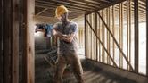 A person wearing safety equipment drills into a wooden beam at a construction site.