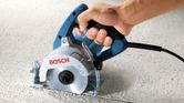 A person guides a marble saw cutting a straight line on a textured stone surface.