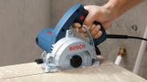 A person cuts marble with a handheld marble saw on a tiled surface.