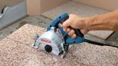 A person guides a marble saw to cut a straight line on a granite slab.