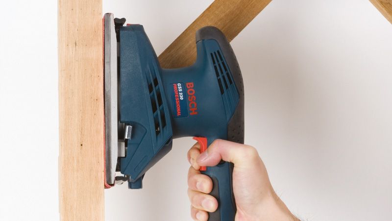 A person uses an orbital sander to smooth a wooden surface.