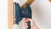 Person using an orbital sander to smooth a wooden beam.