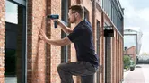 Person wearing safety equipment drills into a brick wall outside a building.