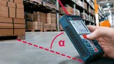 A person uses a laser measure to check distance in a warehouse with stacked boxes.