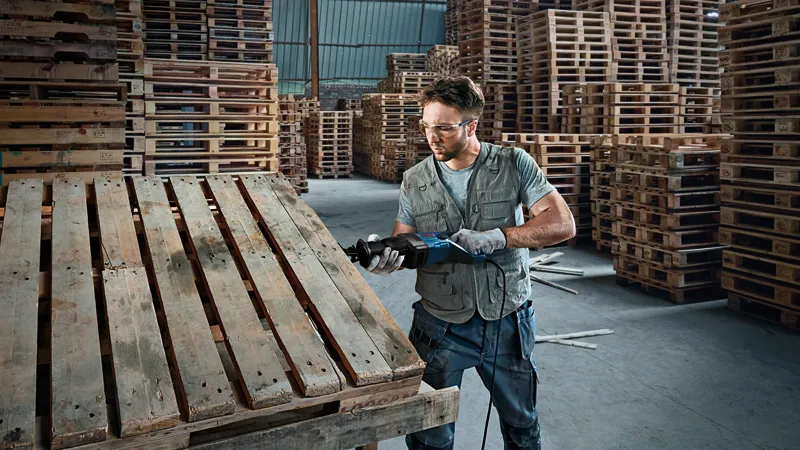 GSA 120 A person wearing safety equipment cuts a wooden pallet using a reciprocating saw.