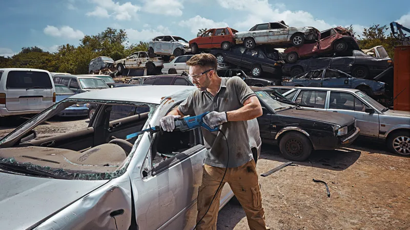 GSA 120 A person wearing safety equipment cuts a car door with a reciprocating saw in a scrapyard.