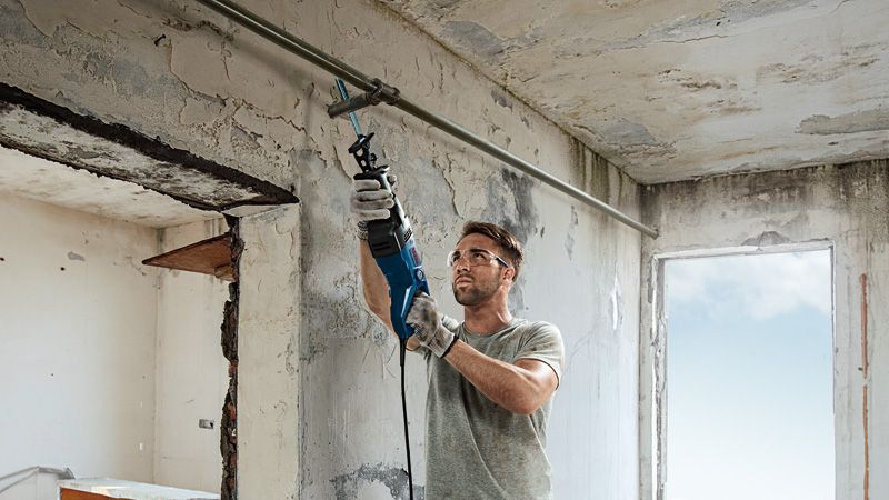 GSA 120 A person wearing safety equipment uses a reciprocating saw to cut a metal pipe indoors.