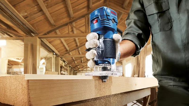 GKF 550 A person wearing safety equipment uses a palm router to shape the edge of a wooden board.