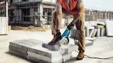A person wearing safety equipment uses a power cutter to cut concrete blocks on a construction site.