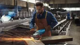 A person wearing safety equipment grinds metal, producing sparks in a factory.