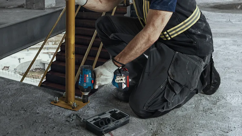 GDS 18V-400 A person wearing safety equipment tightens a bolt on a metal post using a cordless impact wrench.