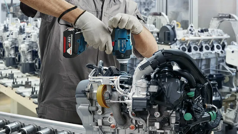 GDS 18V-400 A person wearing safety equipment uses a cordless impact wrench on an engine assembly.