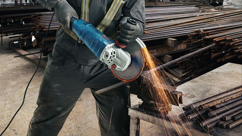 GWS 24-180 JZ A person wearing safety equipment cuts rebar with a large angle grinder, sparks flying.