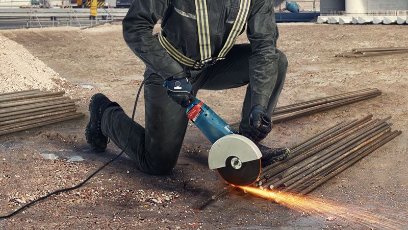 GWS 24-180 JZ A person wearing safety equipment cuts rebar with an angle grinder, creating sparks.