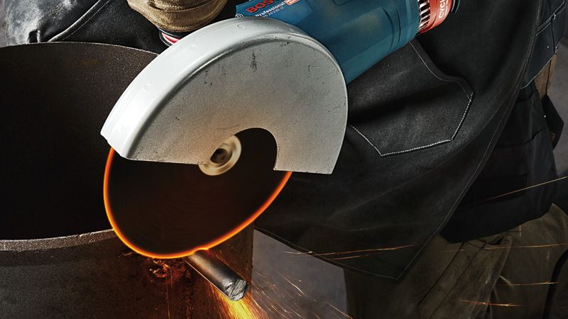 GWS 24-180 JZ A person wearing safety equipment cuts metal pipe with a handheld angle grinder.