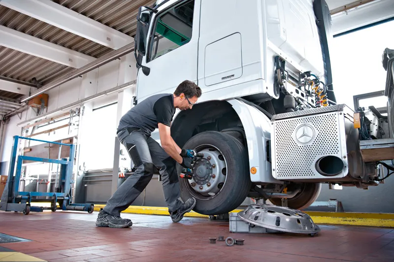 GDS 18V-1000 A person wearing safety equipment uses an impact wrench to remove a truck wheel.