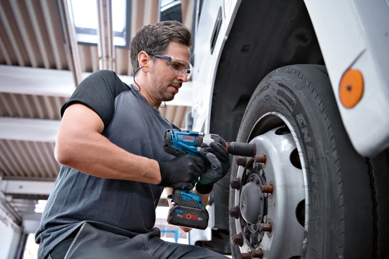 GDS 18V-1000 A person wearing safety equipment uses a cordless impact wrench to tighten truck wheel bolts.