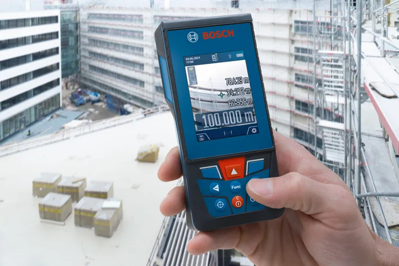 Person holding a laser measure on a construction site with buildings in the background.
